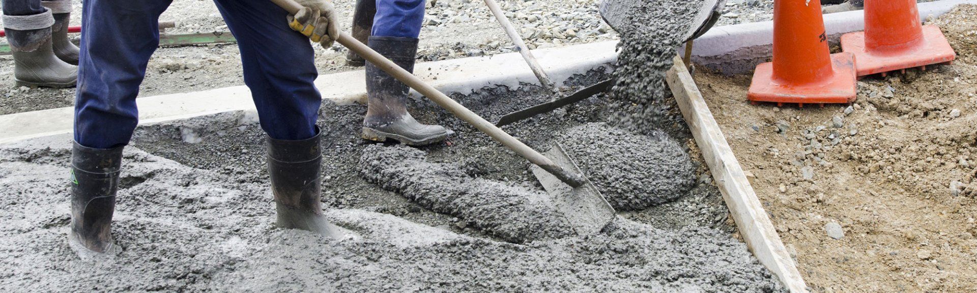 A man is spreading concrete on a sidewalk with a shovel.