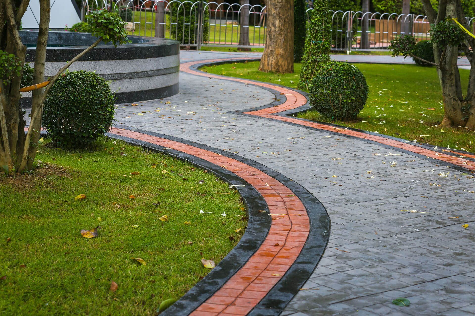 A brick walkway in a park with a fountain in the background.