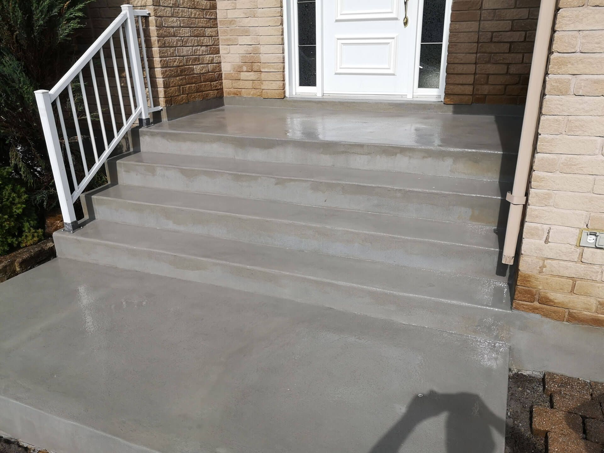 A set of concrete steps leading up to a house with a white railing.