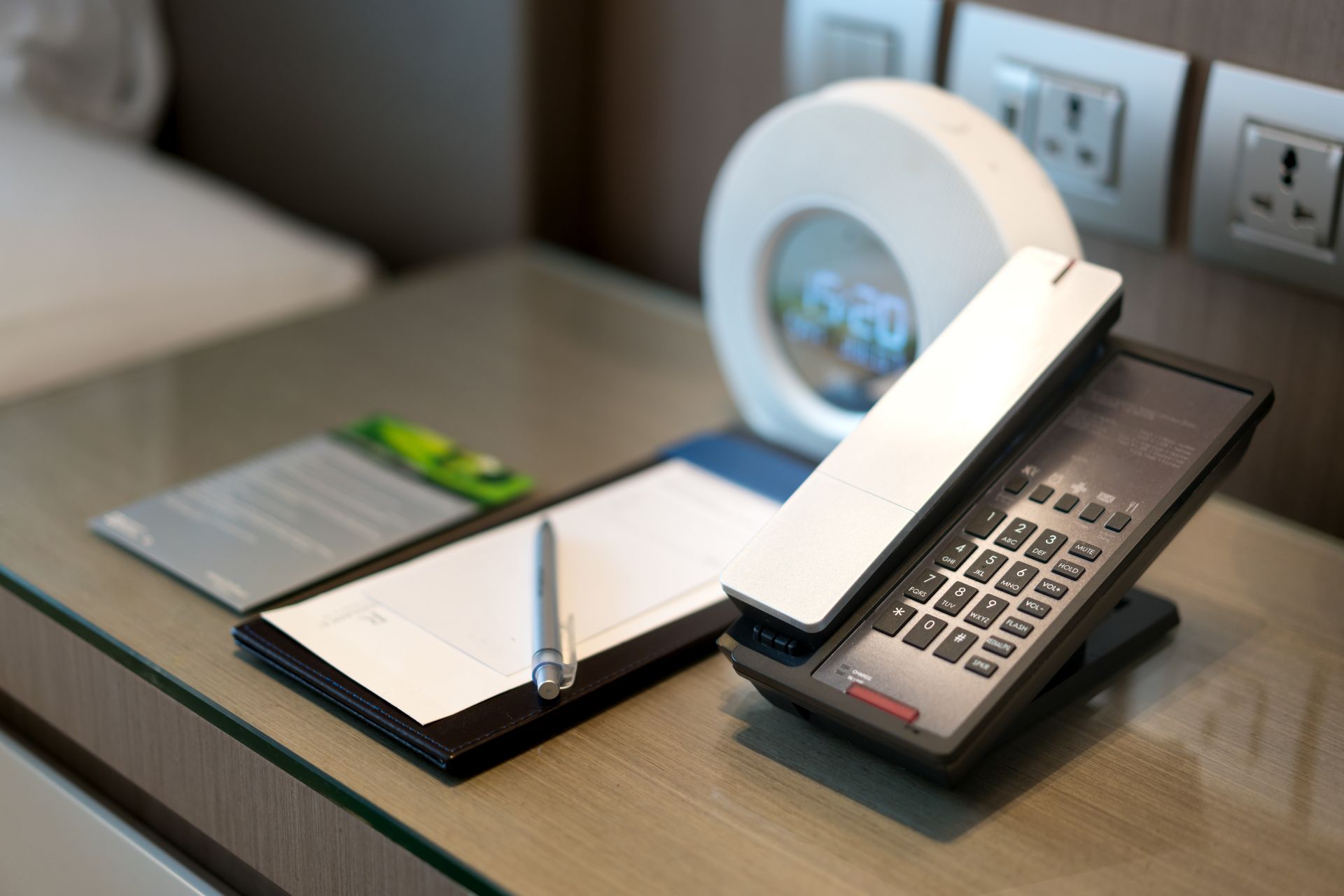 A phone sitting on a glass table next to a notepad and a pen