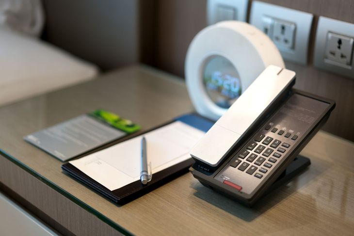 A phone sitting on a glass table next to a notepad and a pen