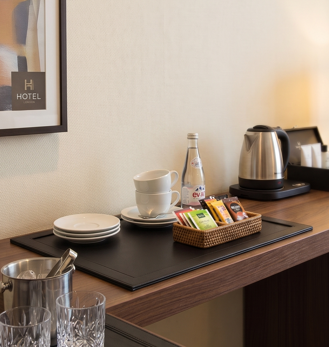 Hotel room coffee and tea setup on a black welcome tray with cups, kettle, snacks, and glasses