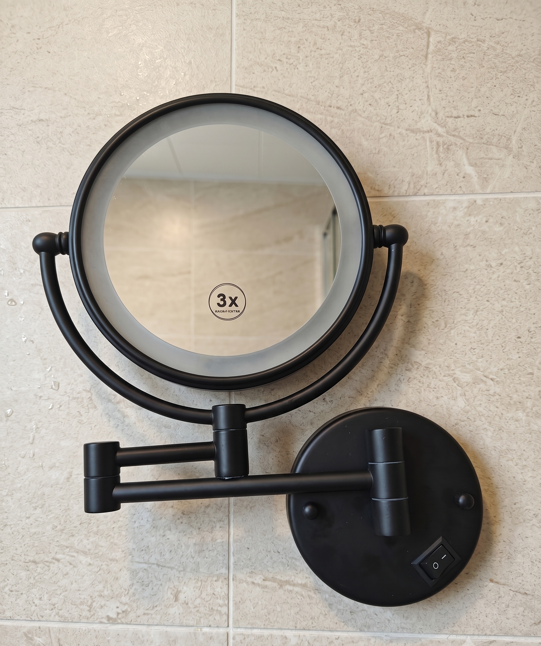Round black wall-mounted magnifying mirror with foldable arm on beige tiled wall