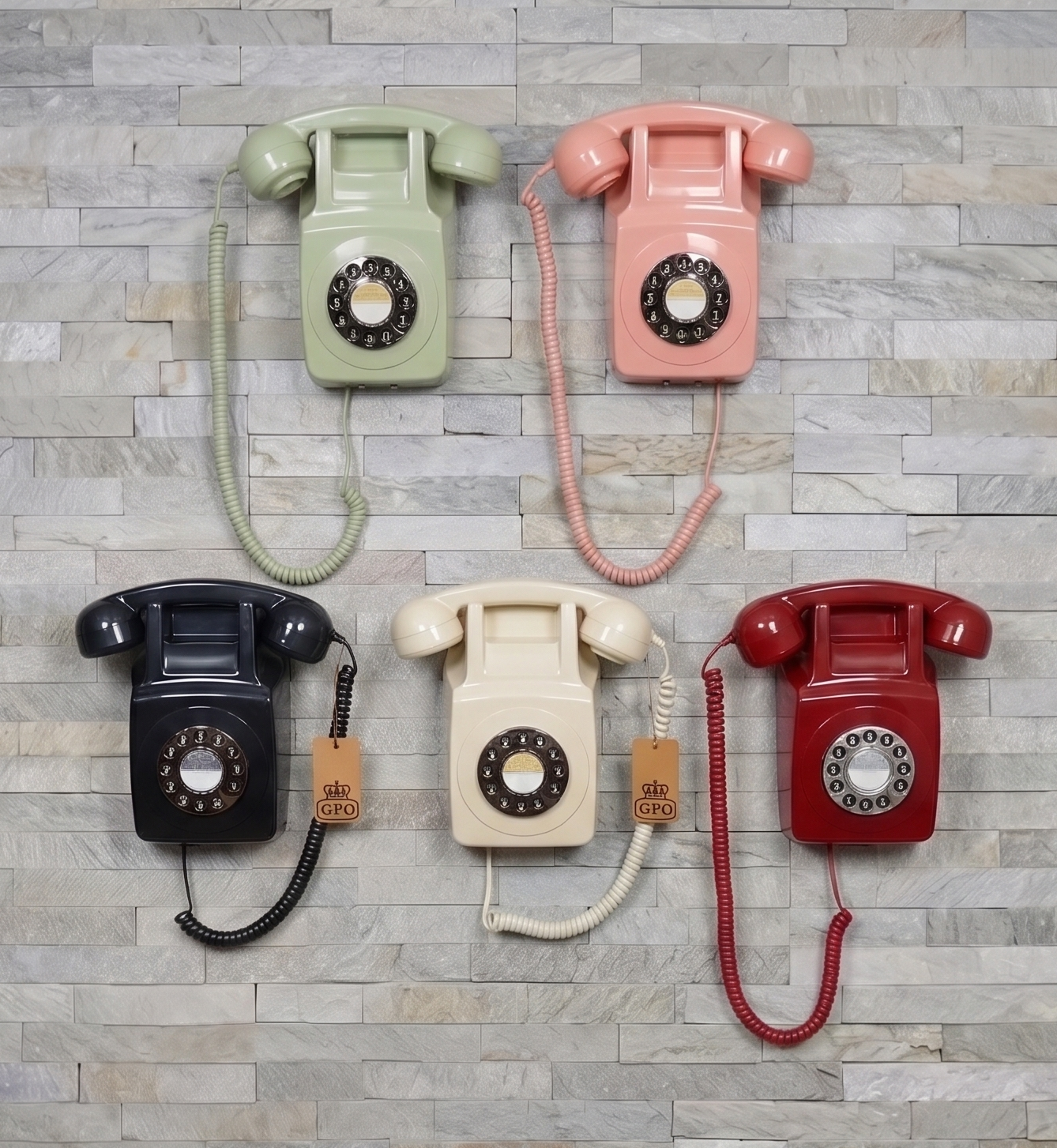 Five vintage wall phones in pastel green, pink, black, cream, and red on a stone wall.