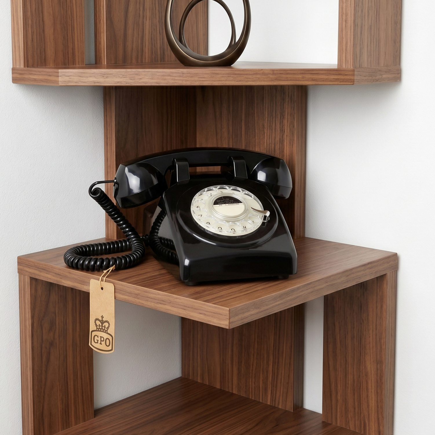 Black rotary phone on a wooden wall shelf with a lower cubby and small hanging tag.