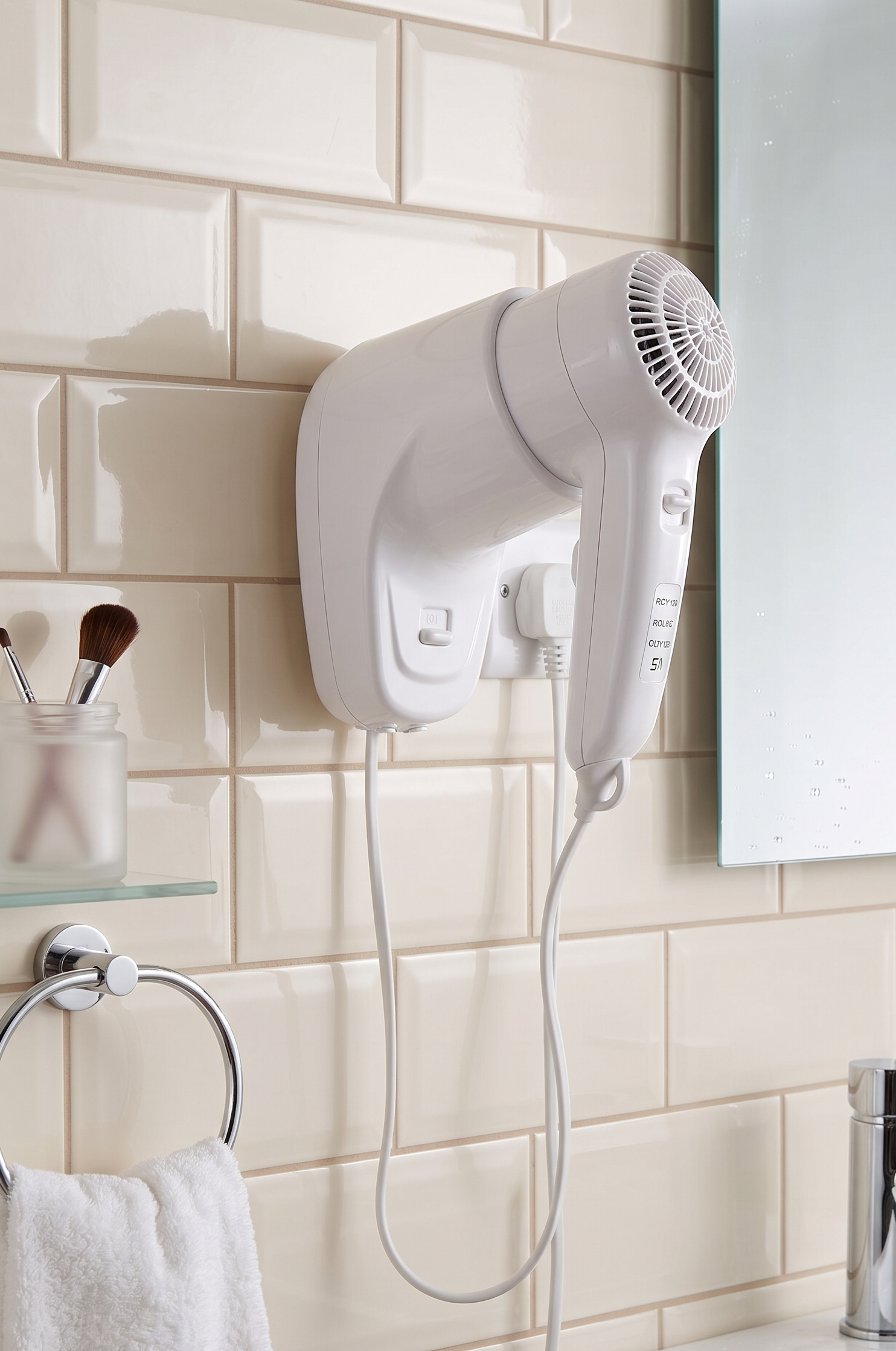 White wall-mounted hair dryer in a tiled bathroom above a sink and towel rack