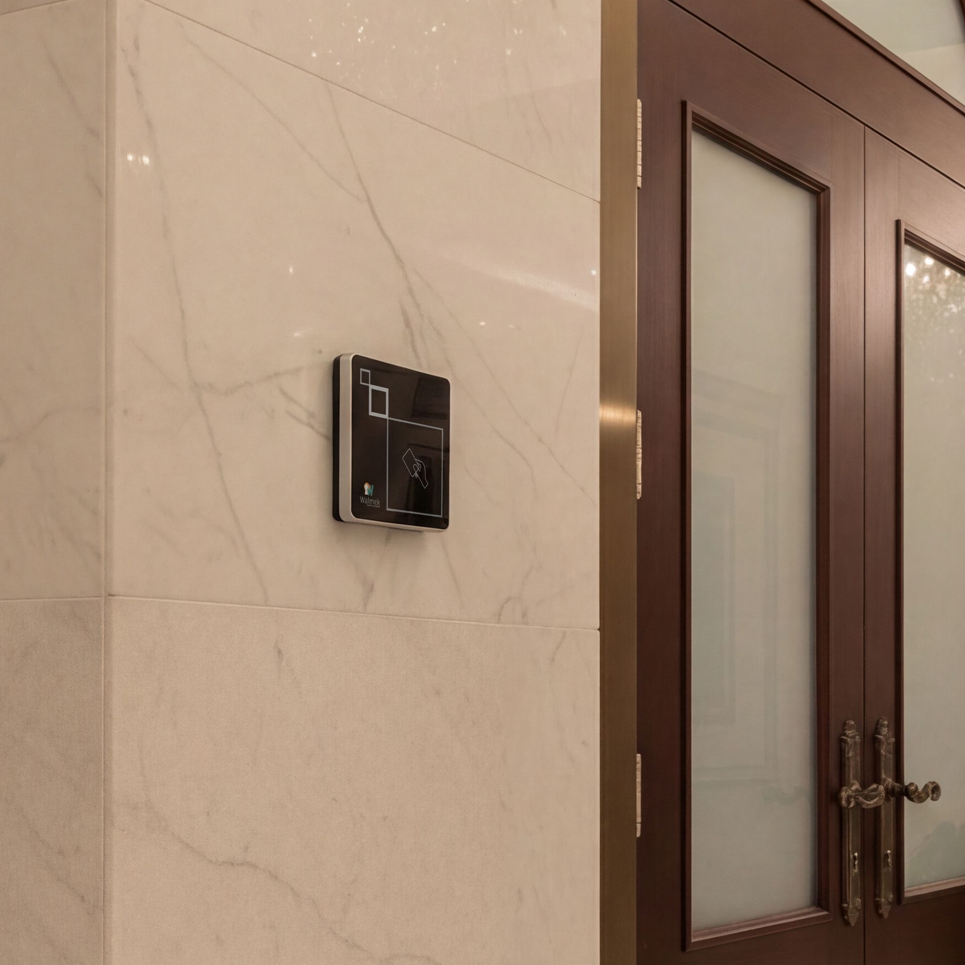 Black wall-mounted control panel on a beige marble wall beside frosted glass doors.