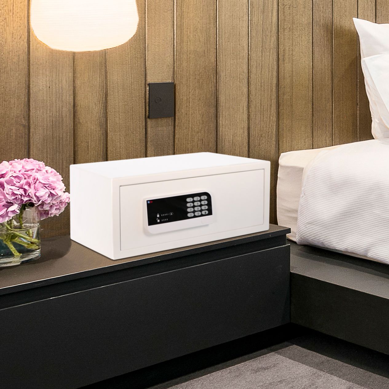 White safe on a black nightstand beside a bed in a wood-paneled bedroom