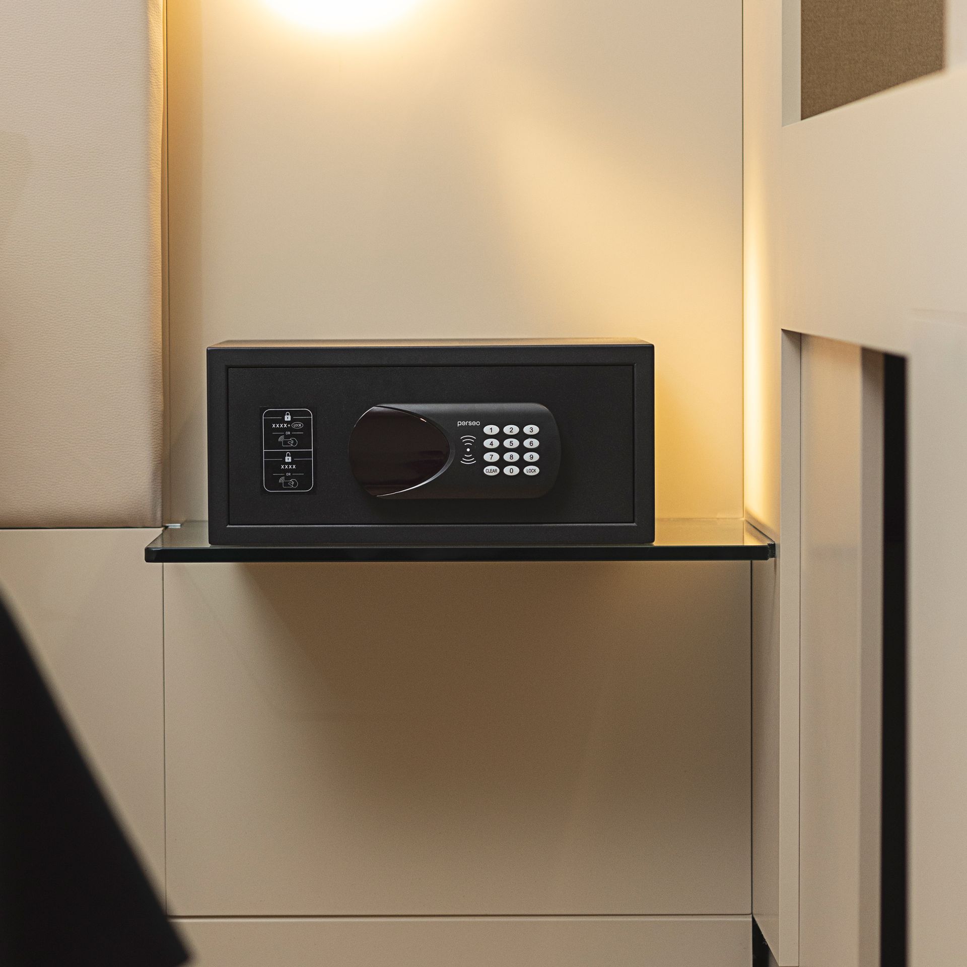 Black digital safe on a beige cabinet in a softly lit room.