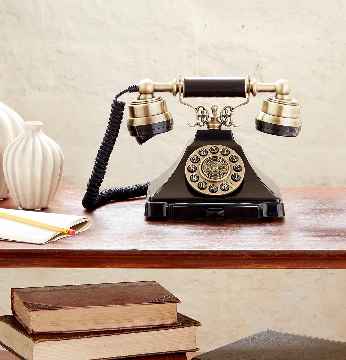 Vintage black telephone on a wooden desk with stacked books and stationery in the background
