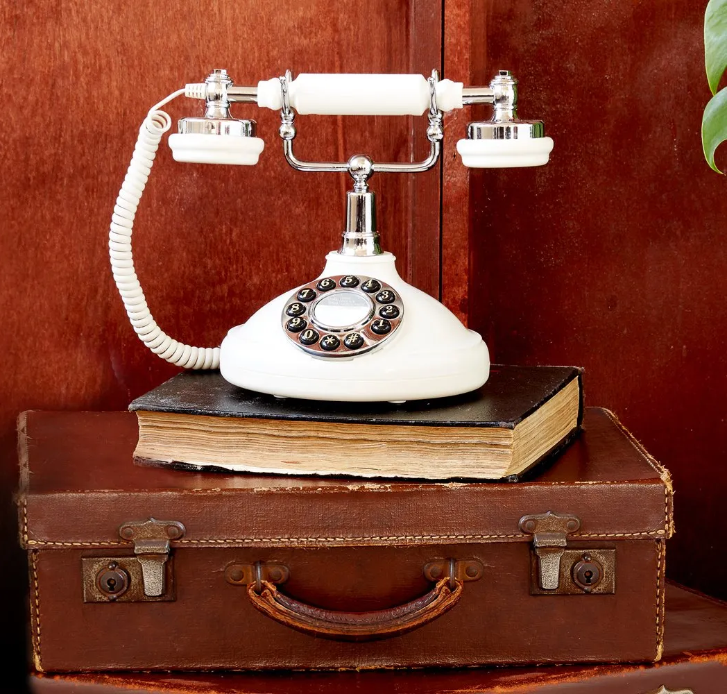 Vintage white phone resting on a leather suitcase with a red wooden background