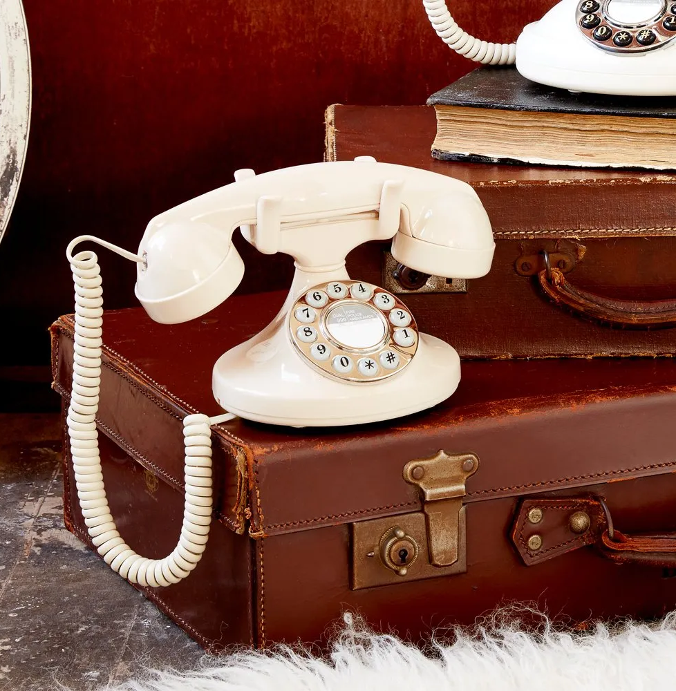 Vintage cream phone on stacked leather suitcases, with another phone partially visible on a book stack.