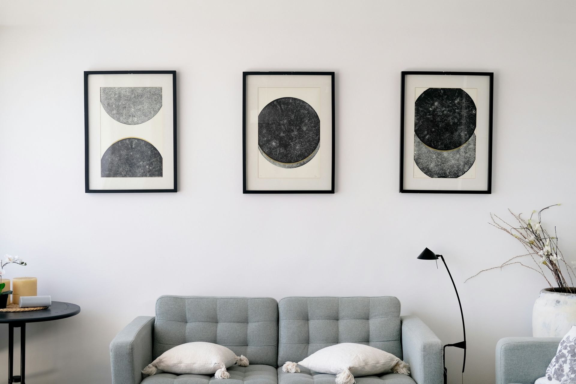 Three framed abstract art pieces above a gray couch. A side table and lamp are on either side.