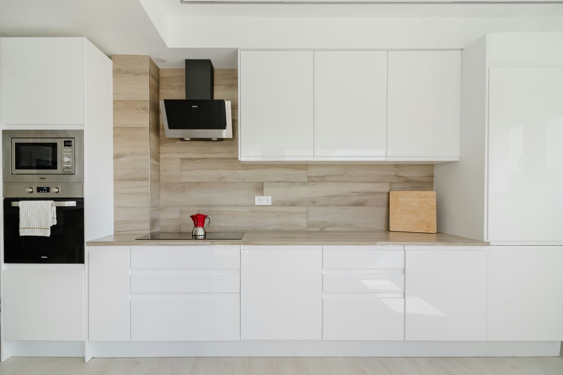 Modern white kitchen with stainless steel appliances, light wood backsplash, and cabinets.