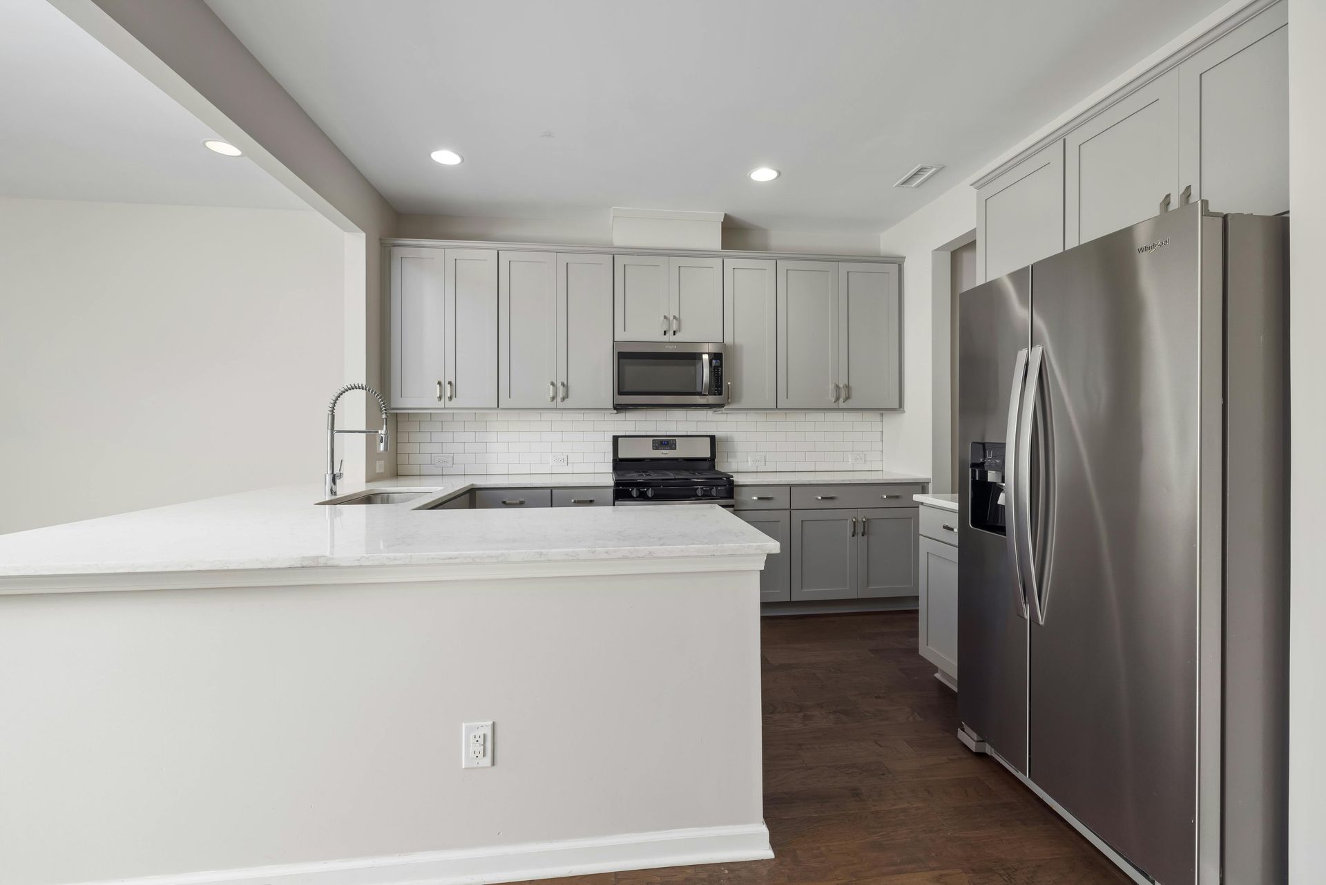 Modern kitchen with gray cabinets, stainless steel appliances, and white countertops.