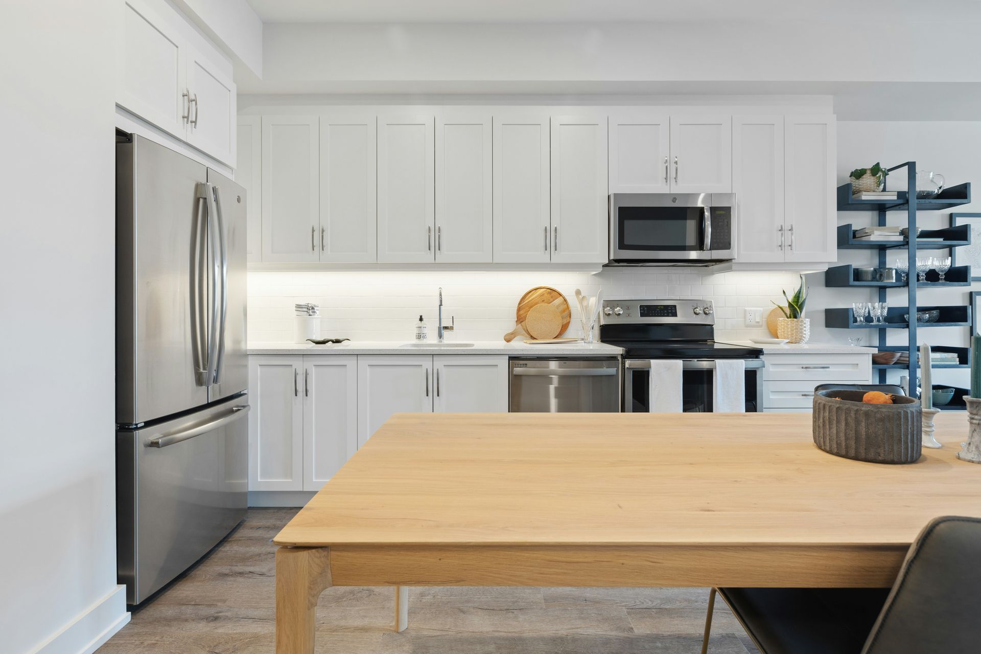 Modern white kitchen with stainless steel appliances, light wood table and cabinets.