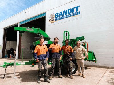 A group of men are standing in front of a bandit tree equipment building.
