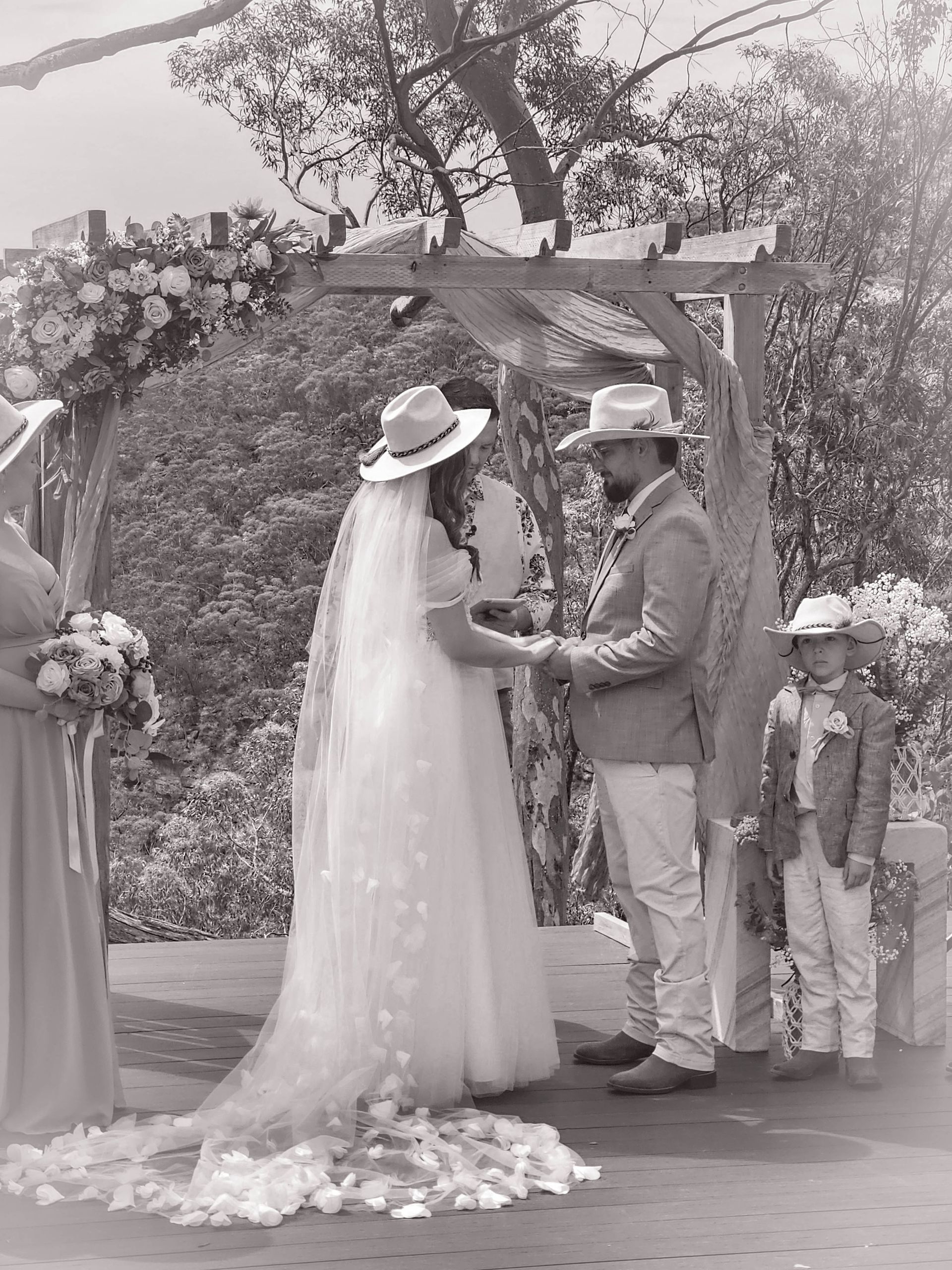 Bride and Groom Exchanging Vows Under a Floral Arch Outdoors, with A Small Child Nearby — Craig Stevens Photography in Pearl Beach, NSW