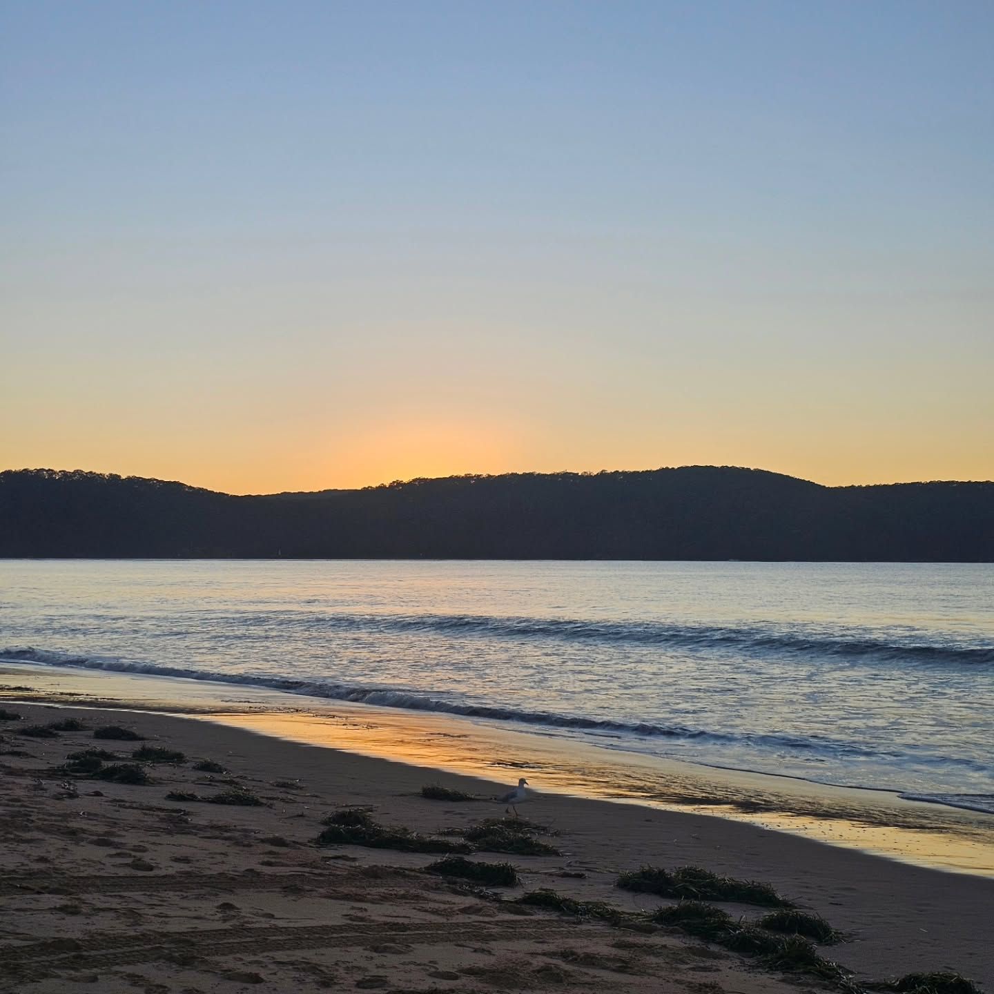 Sunset Over a Calm Beach with Gentle Waves and Silhouetted Hills in The Distance — Craig Stevens Photography in Pearl Beach, NSW
