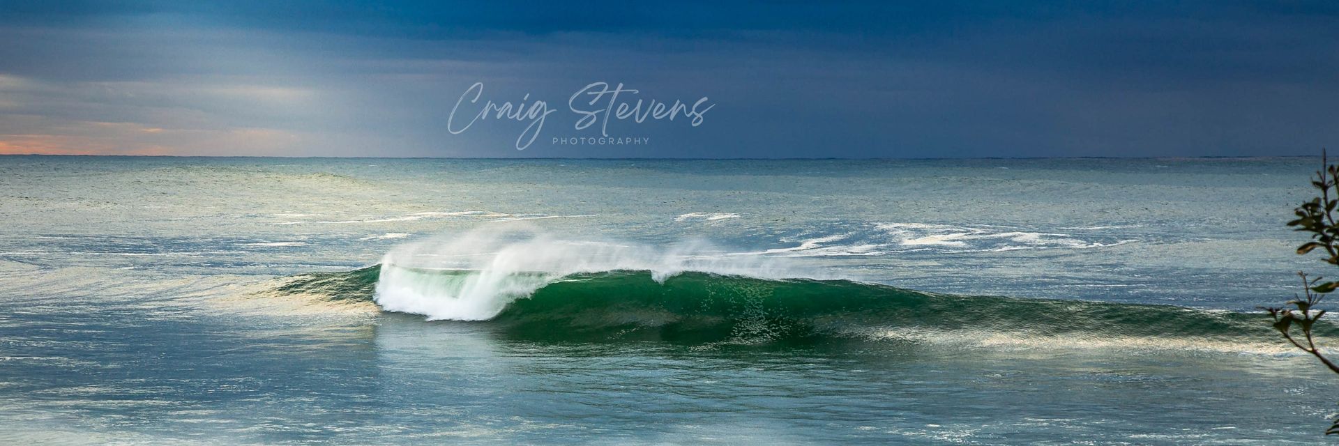 Ocean Wave Breaking on A Sandy Beach Under a Blue Sky, with Faint White Script Near the Top — Craig Stevens Photography in Pearl Beach, NSW