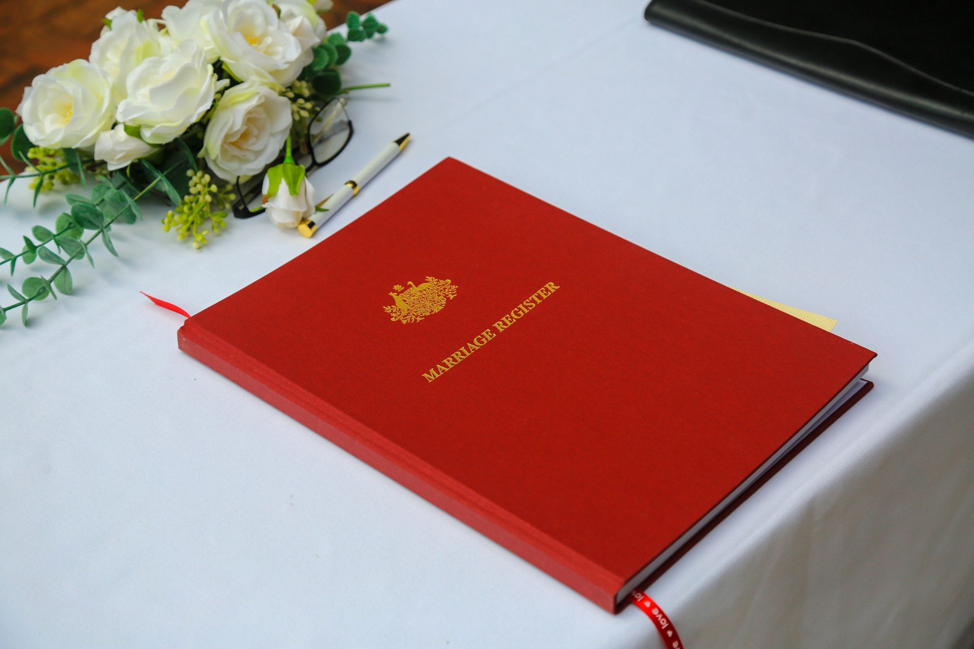 Red Diploma Folder with Gold Emblem on A White Table Beside White Flowers — Craig Stevens Photography in Pearl Beach, NSW