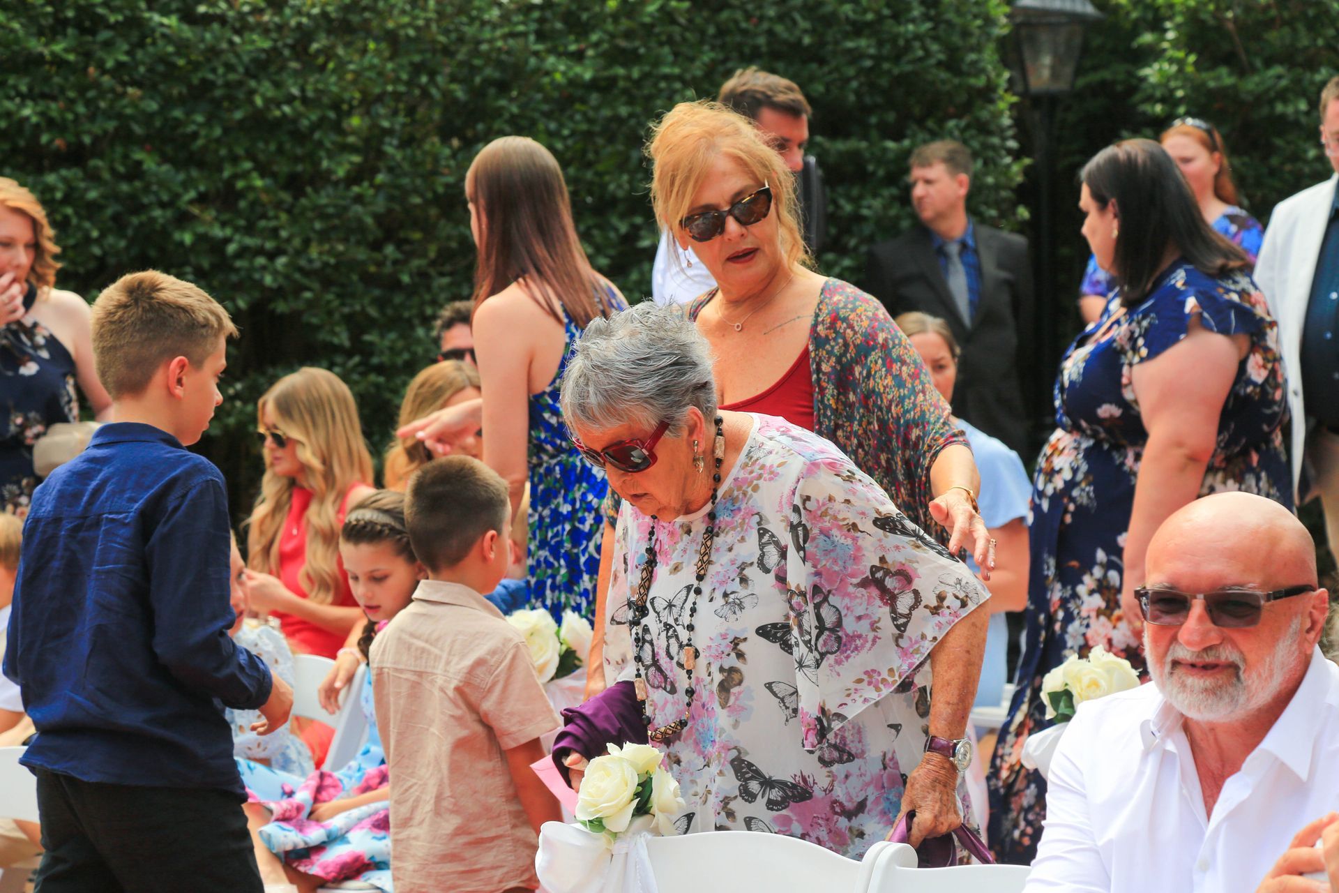 People Gathered Outdoors at A Festive Event, with A Child in Blue and A White Haired Woman Bending Forward — Craig Stevens Photography in Pearl Beach, NSW