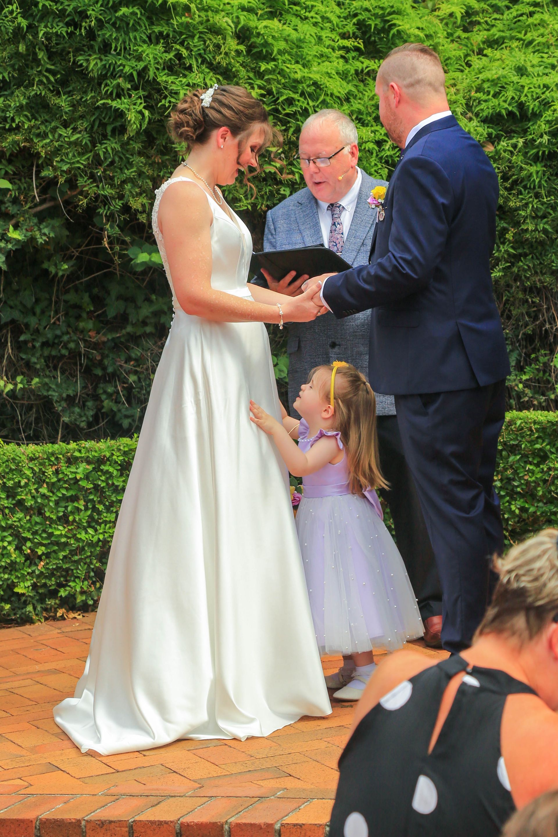 Bride and Groom Exchange Vows Outdoors, with A Child Holding the Bride Dress and An Officiant Beside Them — Craig Stevens Photography in Pearl Beach, NSW