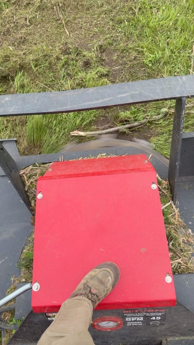 Red platform with a foot on it, viewed from above on an outdoor ride or cart above grass.