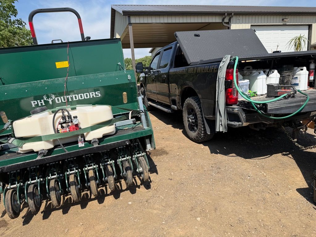 Green agricultural machine beside a black pickup with open tailgate, parked on dirt in a field