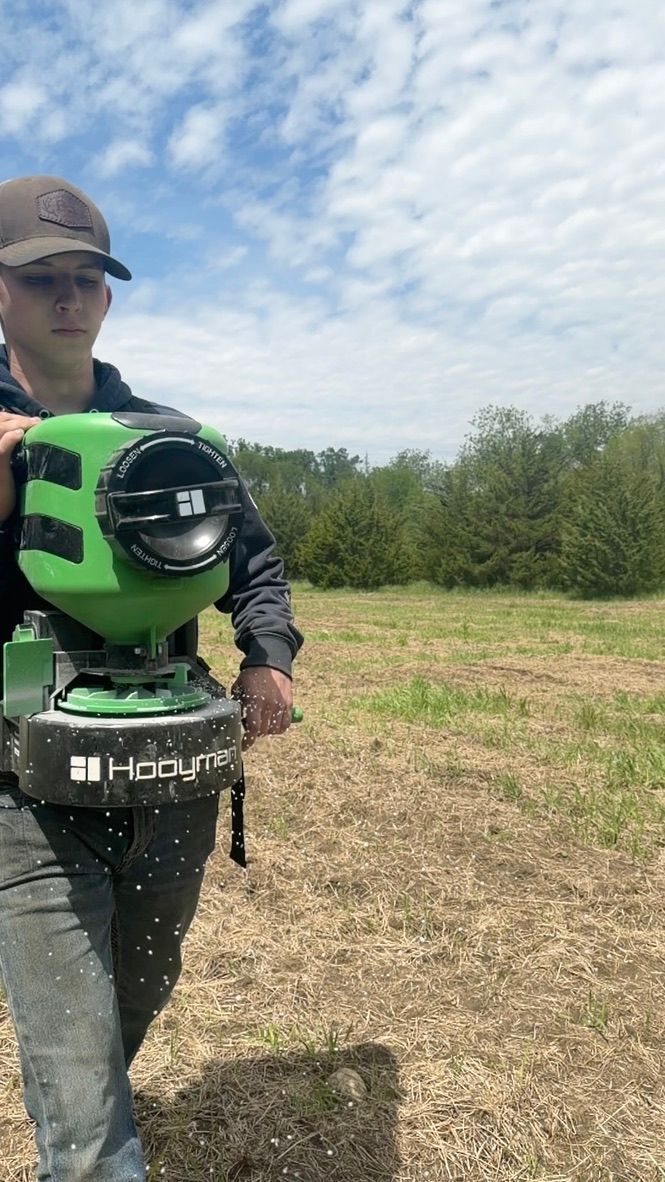Person holding a green-and-black RC vehicle in a grassy field under a cloudy sky