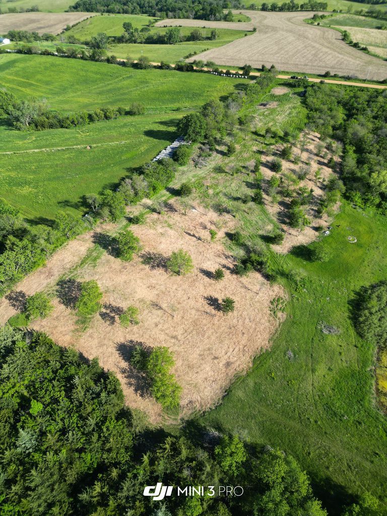 Aerial view of a grassy field with a large tan patch, hedgerows, and farmland beyond.