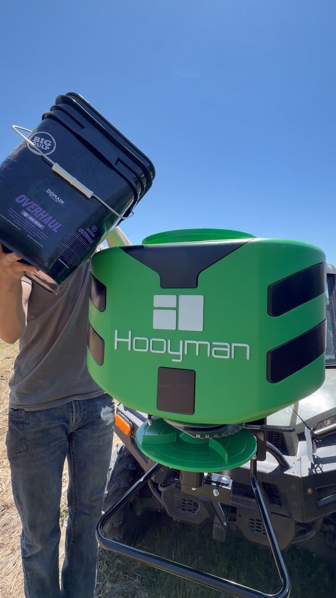 Person holding a blue bag beside a green Hometown machine outdoors under a clear sky