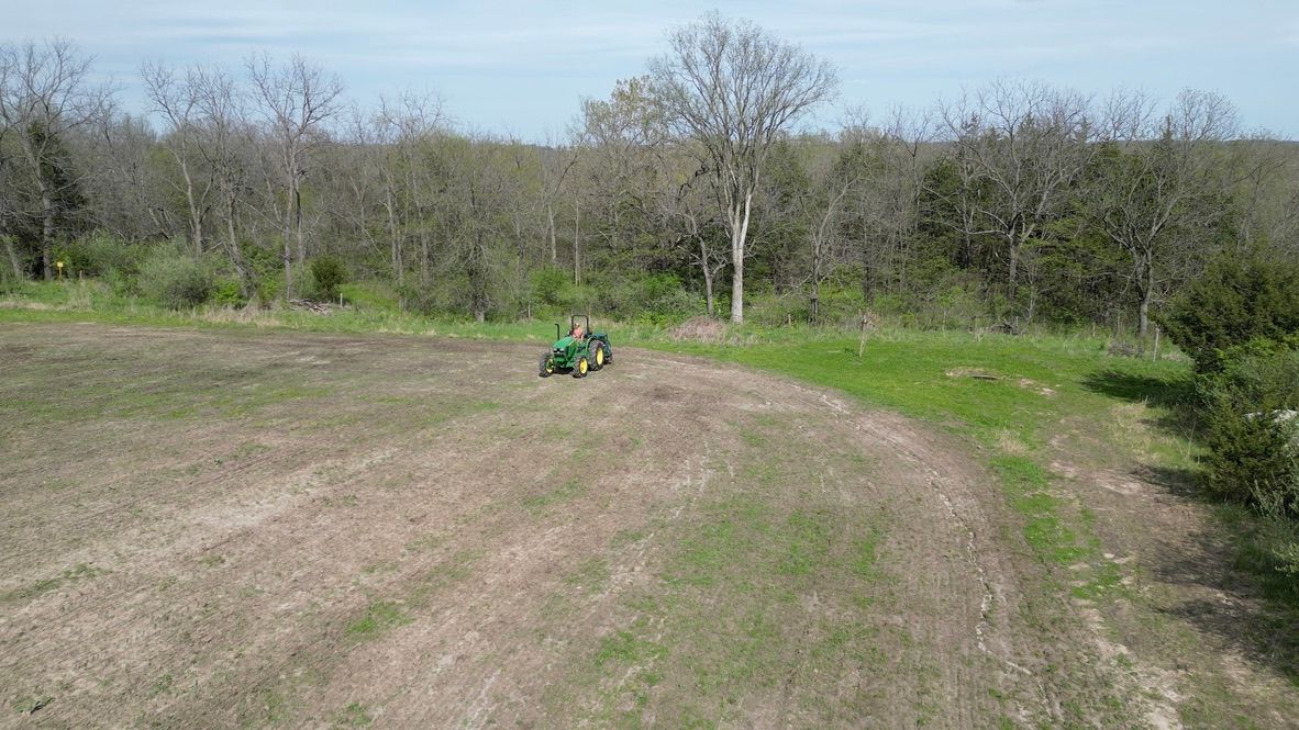Green tractor in a bare field with trees in the background under a clear sky