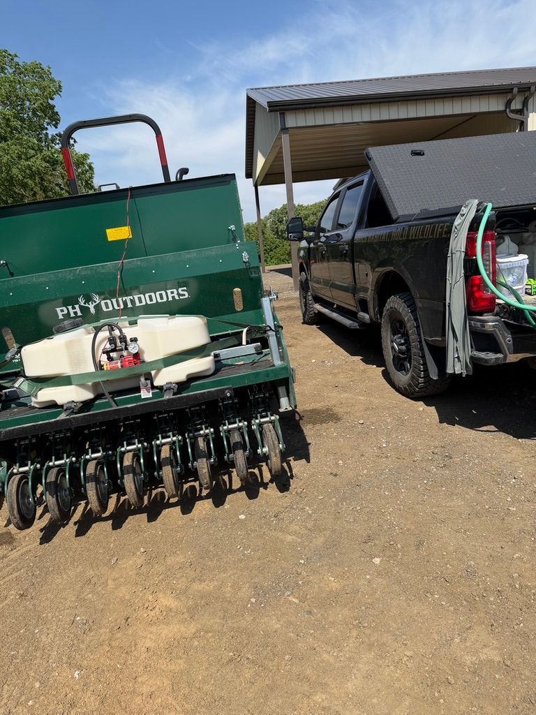 Green farm implement beside a black pickup truck under a canopy on a gravel lot