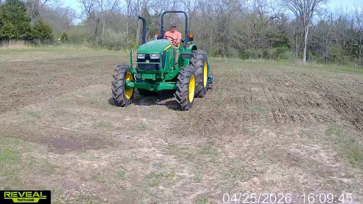 Green tractor mowing a grassy field, with a driver in an orange shirt.