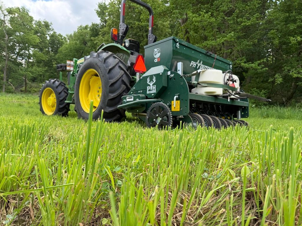 Green tractor with yellow wheels working in a grassy field under trees