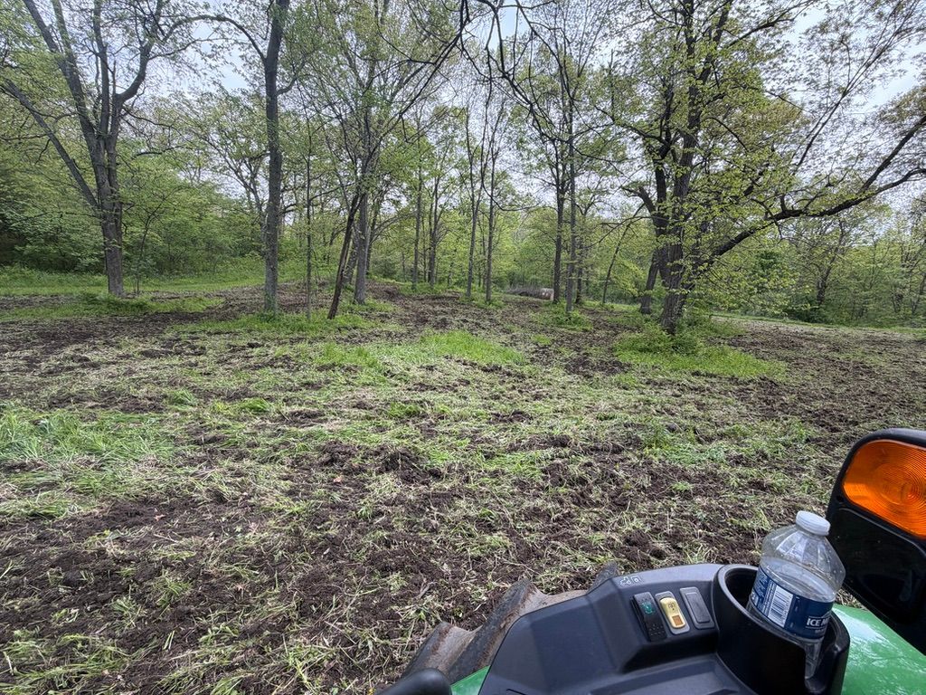 Muddy woodland clearing with trees; ATV dashboard visible in the foreground.
