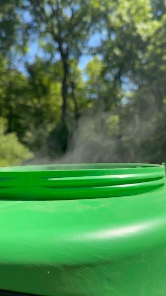 Green plastic lid in the foreground with blurred trees and sunlight in the background