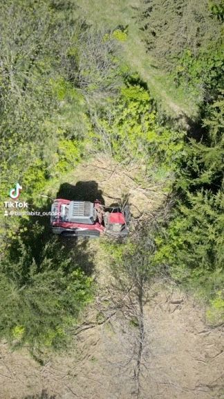 Red off-road truck driving through a narrow dirt path in dense green forest, seen from above