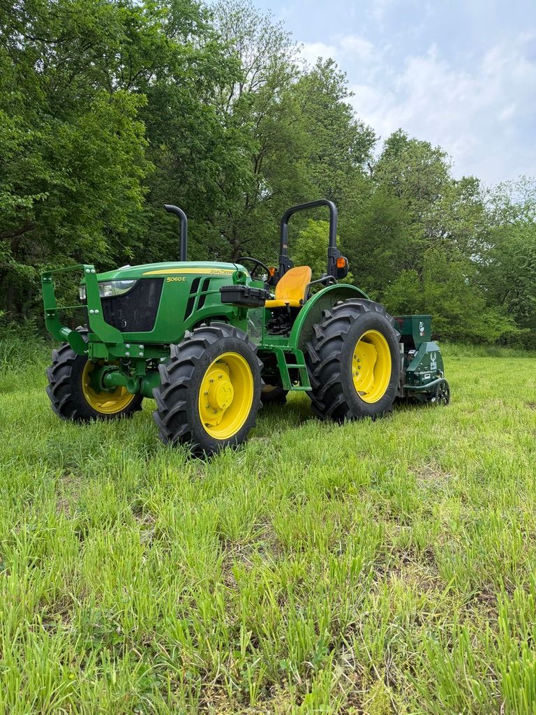 Green John Deere tractor with yellow wheels parked in a grassy field by trees.