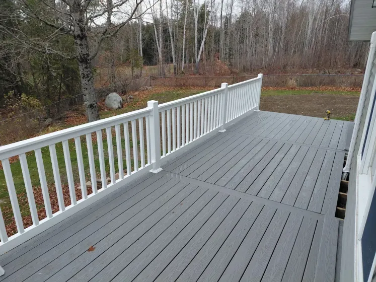Gray deck with white railing overlooking a wooded yard and autumn trees