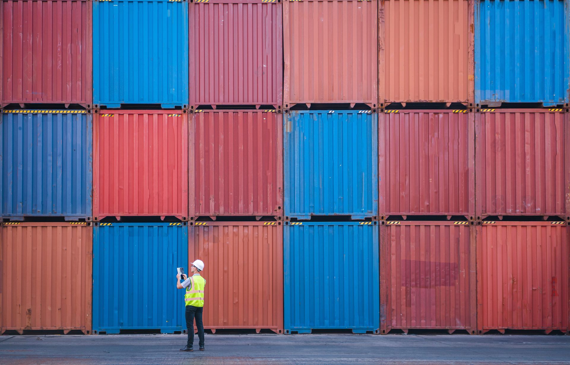 An engineer stands in front of a stack of multicoloured shipping containers. An engineer stands in front of a stack of multicoloured shipping containers.