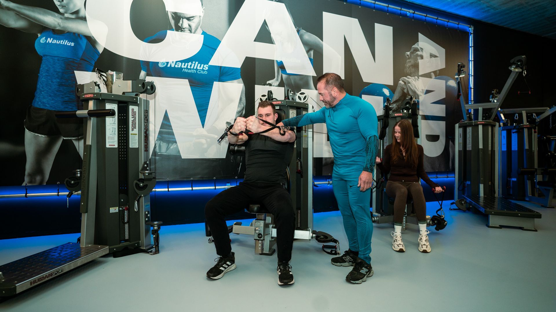 Mensen poseren in een sportschool met blauwe apparatuur en een grote