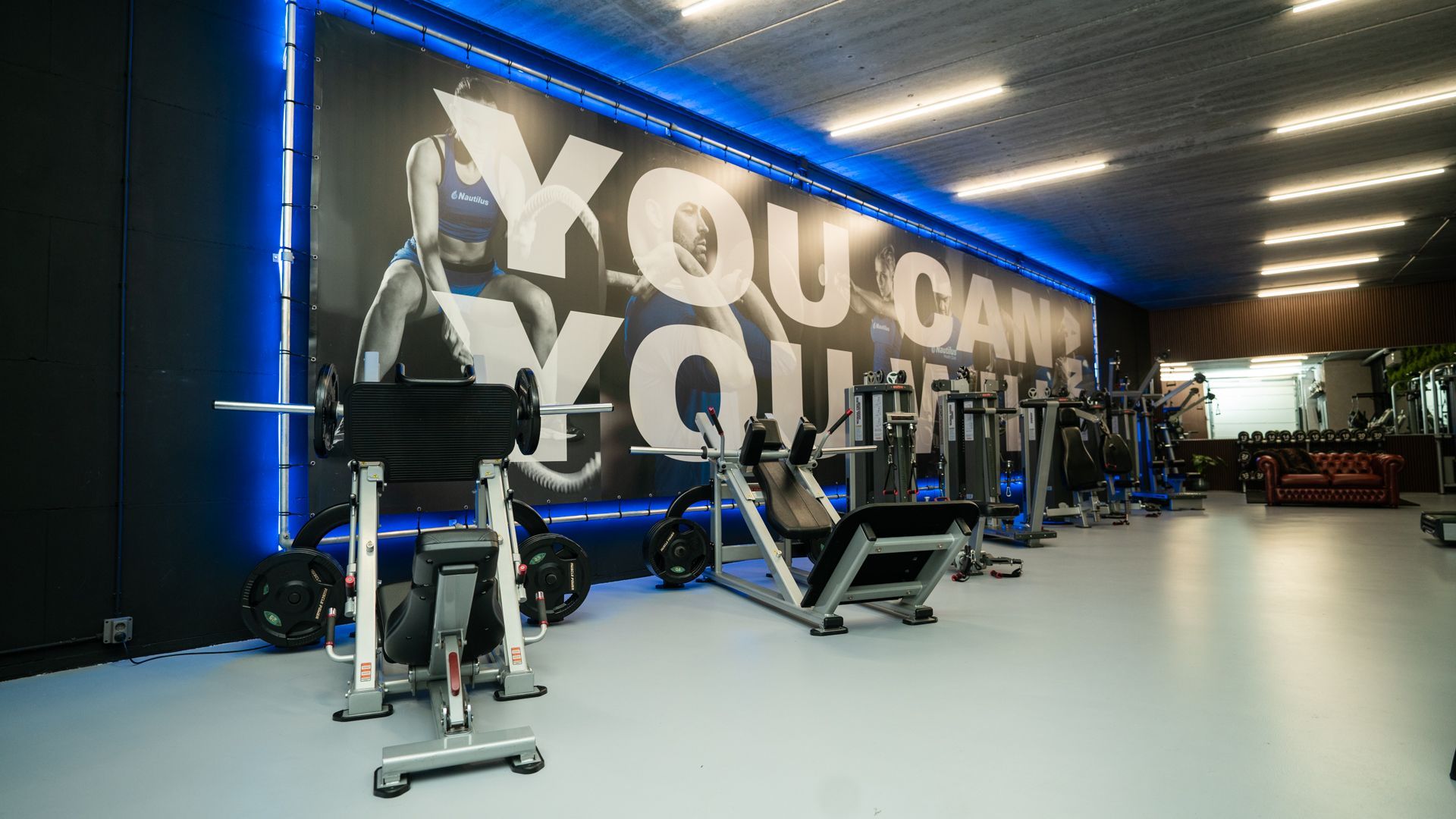 Moderne sportschool met hometrainers, blauwe verlichting en een grote muurtekst met de woorden