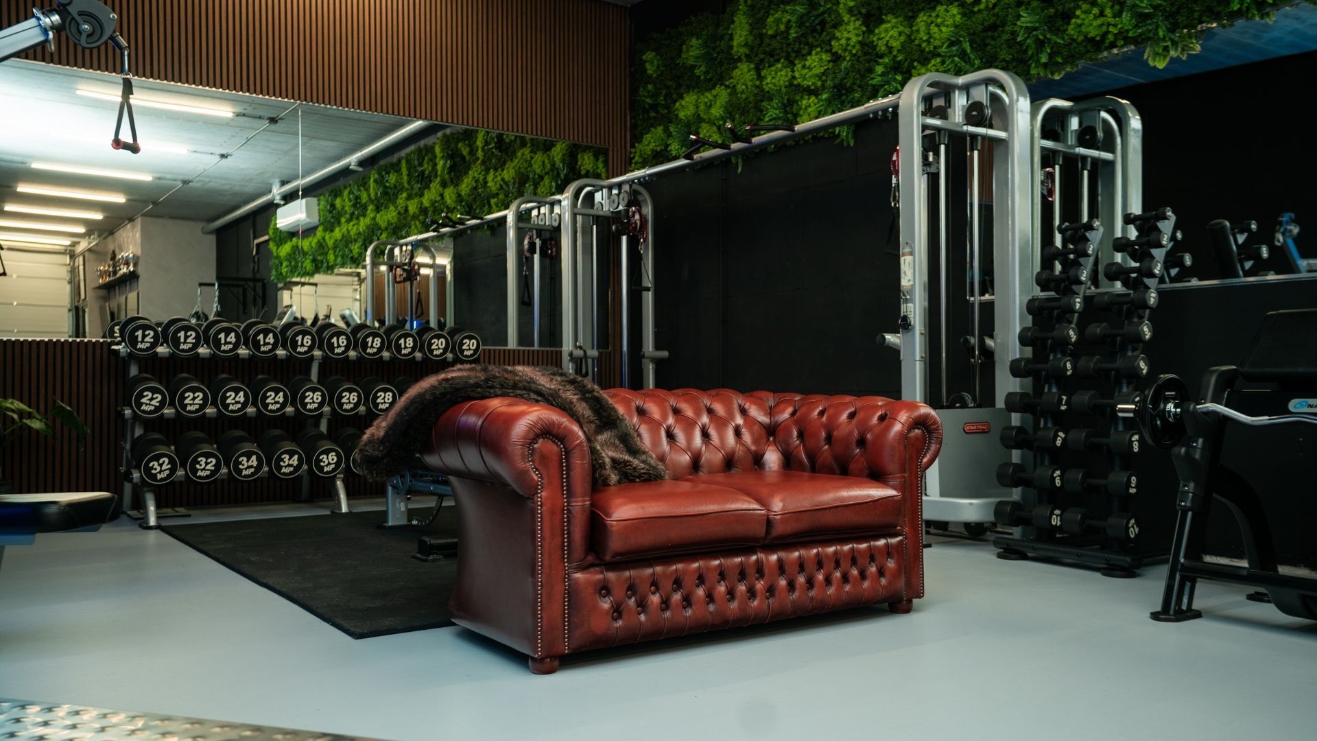Rode leren bank in een moderne sportschool met gewichtsapparaten en dumbbells op de achtergrond.