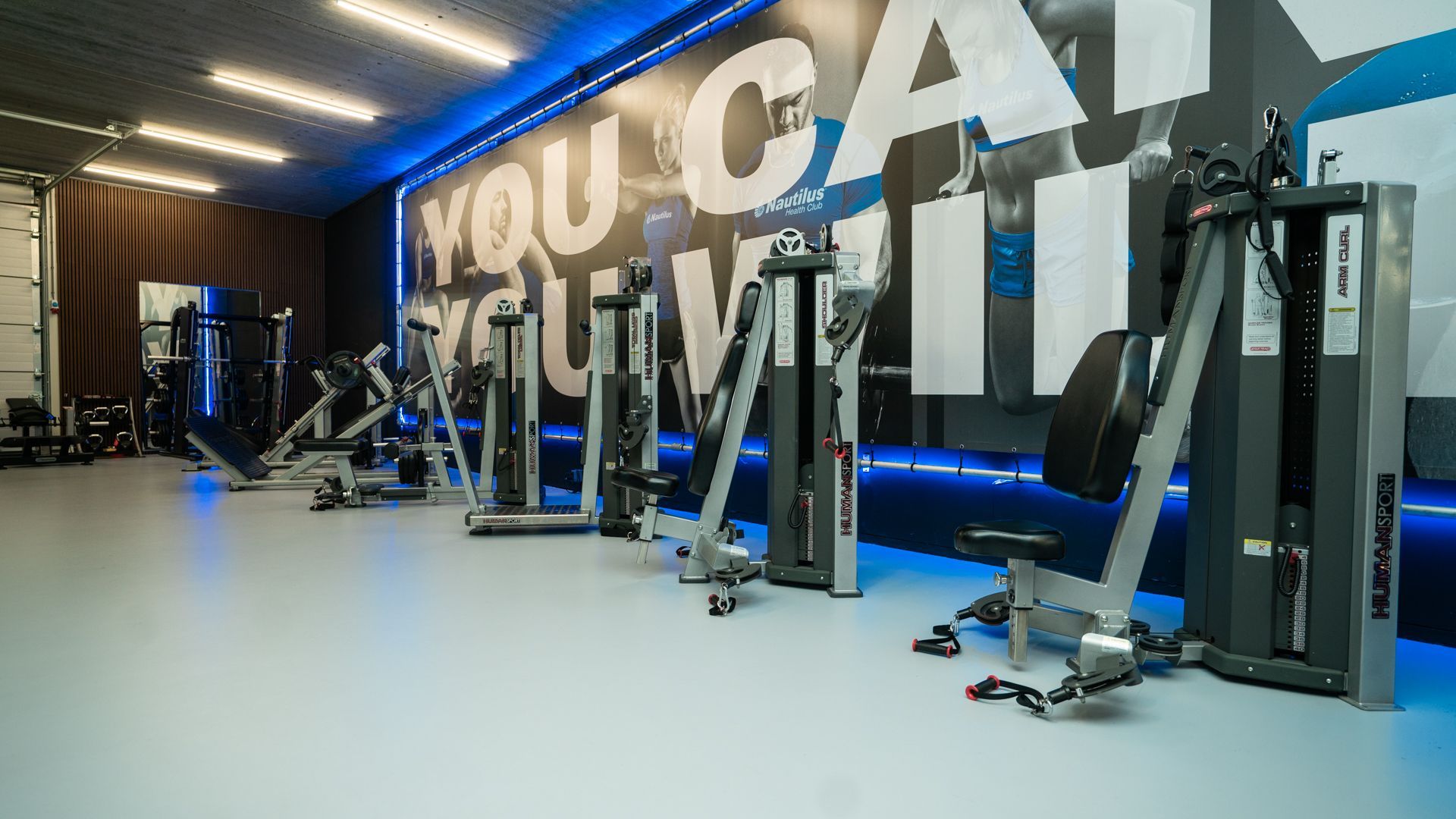 Modern fitnesscentrum met fitnessapparaten, blauwe accentverlichting en grote muurteksten met de tekst