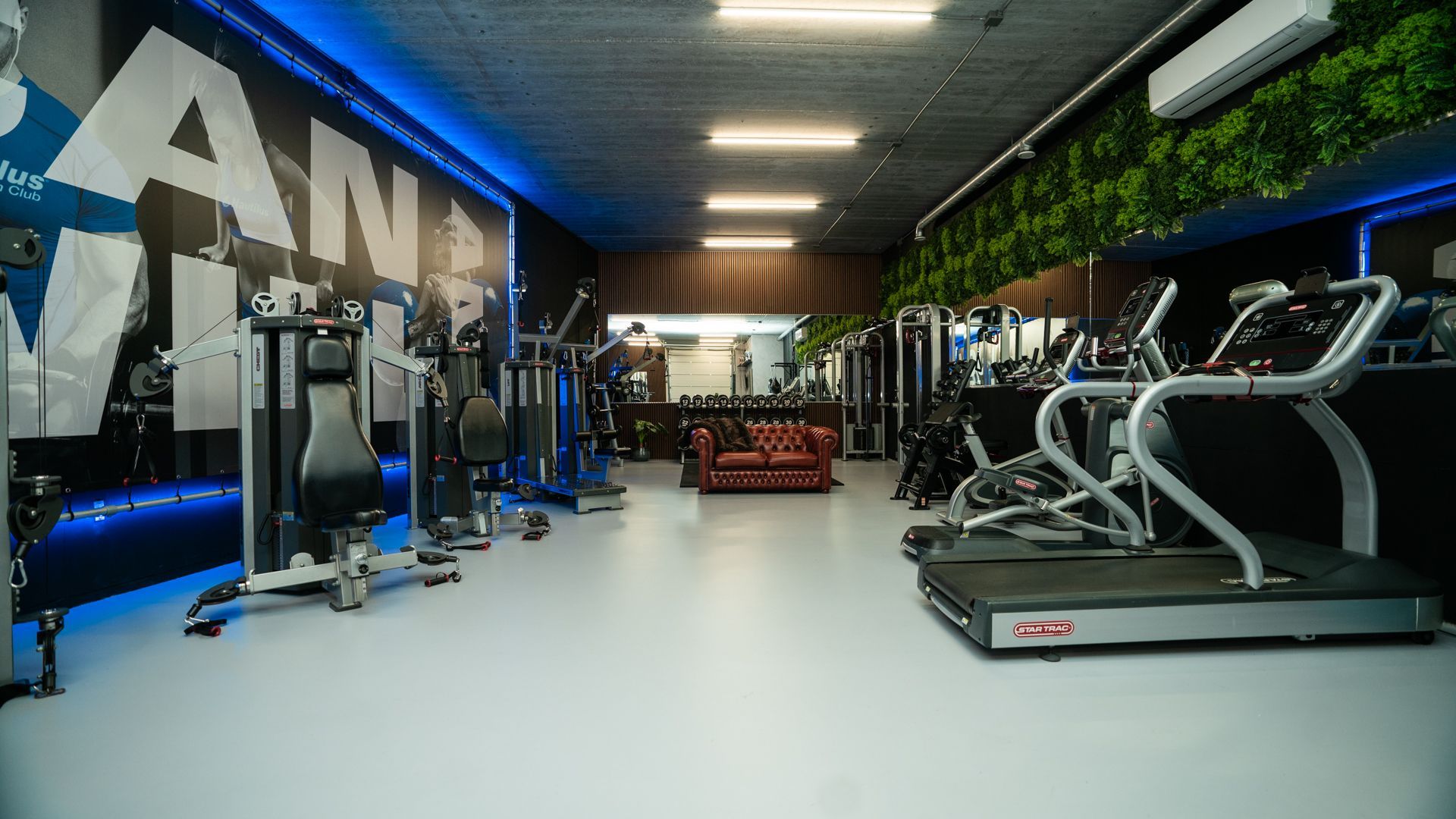 Modern fitnesscentrum met loopbanden, gewichtsapparaten en blauwe accentverlichting.