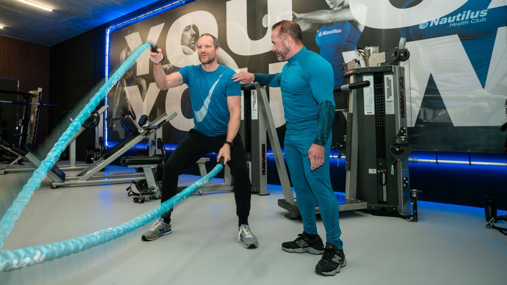 Vrouwen boksen in een sportschool, een van hen slaat op een bokszak, de ander slaat op stootkussens met een coach.