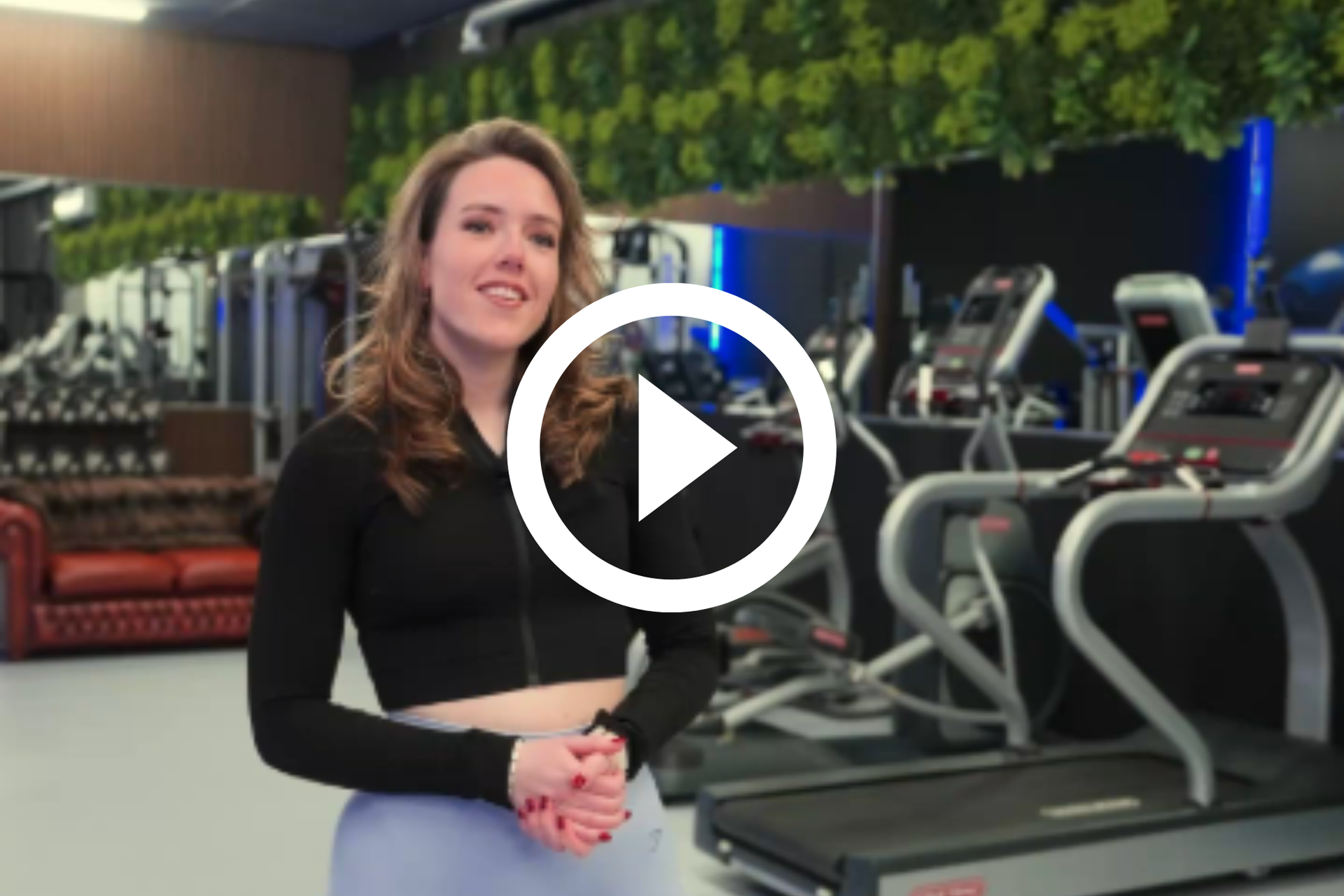 Vrouw staat lachend in een sportschool naast loopbanden en fitnessapparatuur.
