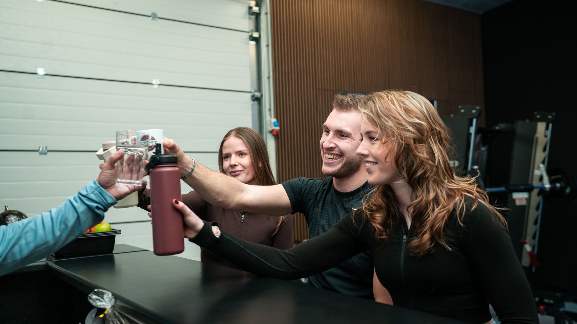 Mensen klinken met hun drinkflessen in een garage, lachend en feestvierend.